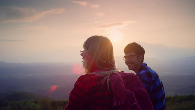 Two young adults, a girl and a boy, watched the mountain panorama at sunset with delight, handheld shot. Leisure, outdoor activity and adolescence concepts.