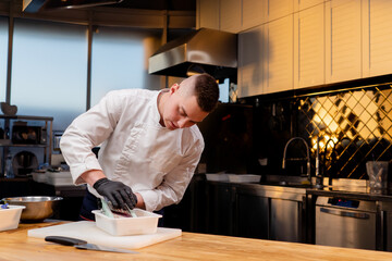 a chef in the kitchen in a white jacket grates beets on table in a buck