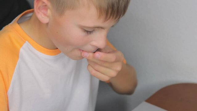 a boy in a white T-shirt sits at the table peeling and eating peanuts
