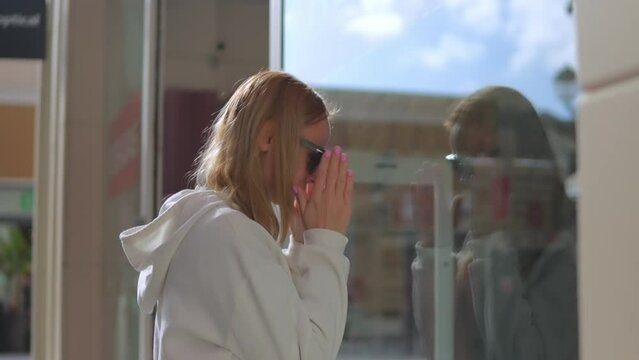 Shopping of a young beautiful woman. The blonde stands near the display case