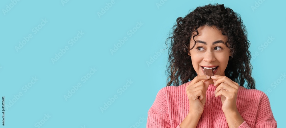 Canvas Prints beautiful young african-american woman eating piece of sweet chocolate on light blue background with