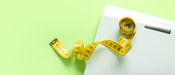 Scales and measuring tape on green background with space for text, closeup. Weight loss concept