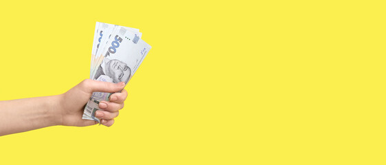 Female hand holding Ukrainian hryvnia banknotes on yellow background with space for text