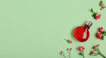 Bottle of perfume and beautiful flowers on green background with space for text