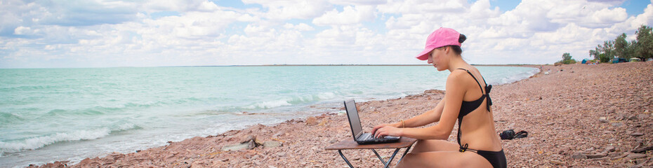 a girl in a sexy swimsuit working at a table on the ocean surf, working remotely from the office,