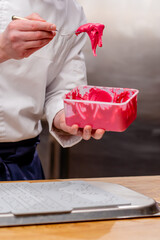 close-up of a chef's hand taking a pink stretchy spread for decoration with spoon