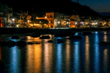 Fototapeta na wymiar night town coast with flashlights from embarkment and reflection in sea gulf water with golden urbal lights and blue hour sky on background of landscape