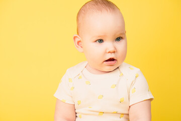 Portrait of happy baby girl on yellow background. Pretty infant looking away, smiling.