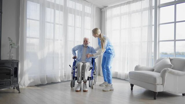 Nurse helps old wheelchair man to walk. Physical therapist woman provides medical support to senior male training studying to go. Recuperation after trauma, injury, temporary paralysis concept.