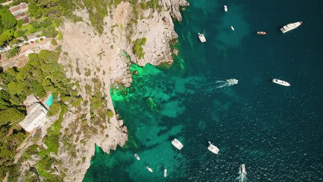 Coastal Aerial Landscape with Boats and Rocky Cliffs in summer lush greenery. Iconic sea stacks Faraglioni emerge from azure waters of Capri, Italy.