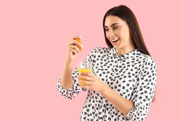 Young woman with glass of juice and orange on pink background