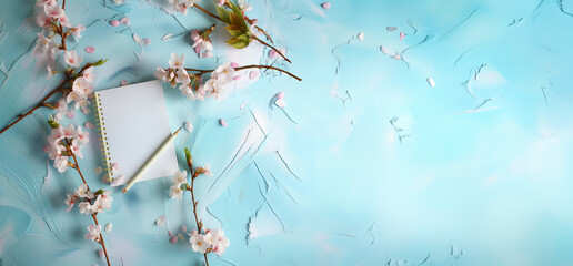 cahier ou bloc-notes, mock-up, avec des branches de fleurs de cerisier autour, sur un fond texturé à la peinture, bleu clair et blanc avec espace négatif pour texte, copyspace