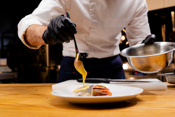 close-up of a chef's hands holding a bowl and pouring sauce from a spoon onto the finished dish