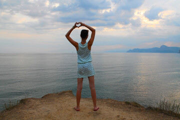 A teenage girl shows a heart made of palms, sunset, silence, tranquility, clear sky and a flat horizon line