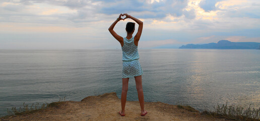 A teenage girl shows a heart made of palms, sunset, silence, tranquility, clear sky and a flat horizon line
