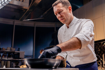 bottom shot of a chef trying to turn a fish fillet on hot frying pan with his hand