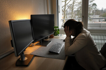 Stressed woman working on her home computer, holding her head