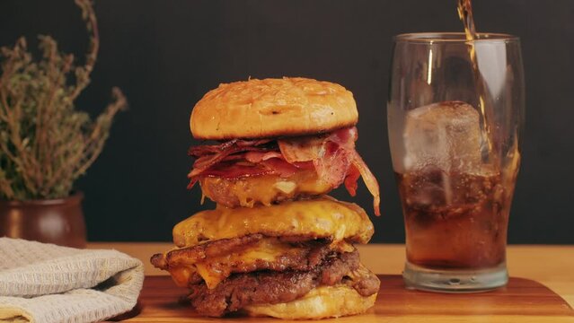 American fat smash burger with bacon slices and cheese on grill and grilled potato slices, with fresh ice coke close-up . Beef or pork cutlet smashing by burger press. The