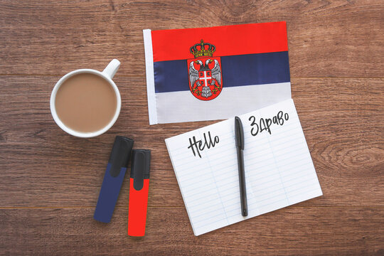 serbian national flag, cup of coffee, notebook with the inscription hello in serbian, two markers on the desktop, flat way, concept of learning foreign languages