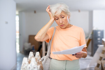 Stressed mature woman homeowner examining room under reconstruction, having problems with documents...