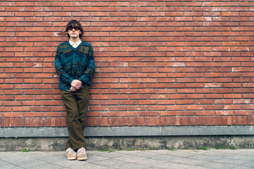Young hipster wear in 90s fashion style stand against red brick wall in urban environment, copy...