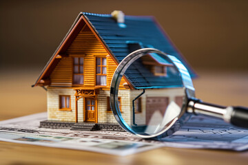 Home inspection concept, inspecting a house, buying a new house, house evaluation, real estate market, a miniature house and magnifying a glass