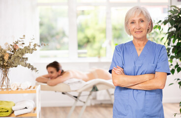 Fototapeta premium In spa office there is elderly woman nurse dressed in medical uniform, suit. Advertising poster, banner for salon of cosmetology and massage services