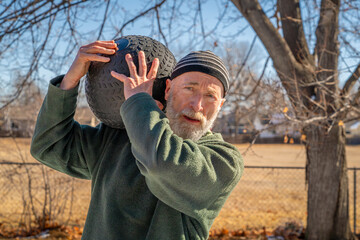 senior man is exercising with a heavy, 50 lb, slam ball in his backyard, sunny winter day
