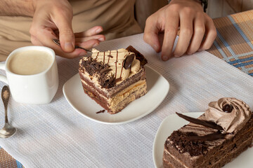 Young man eats tiramisu cake with teaspoon. Close-up of men's hands during breakfast in kitchen. On...
