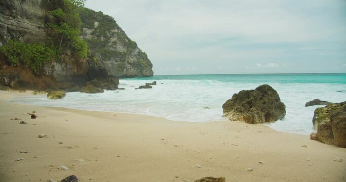 Secluded beach with azure waters. A serene sand shore by steep cliffs and clear, turquoise ocean waves.