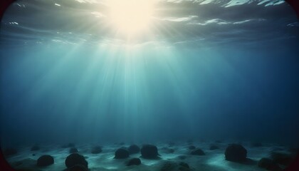 Naklejka premium Sunlight filtering through the surface of the ocean with a seabed covered in rocks