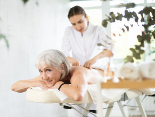 Obraz na płótnie Canvas Unrecognizable blurred female masseur performs massage shoulder area to senior woman. Therapeutic restorative massage.