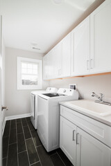 A laundry room with dark grey tiled floor, white cabinets and appliances. No brands or labels.
