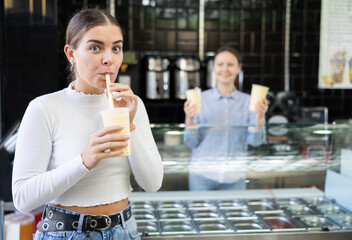 Young girl standing beside bubble tea display, savoring taste of popular Taiwanese refreshing beverage in disposable cup ..