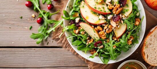 Green apple salad with rocket, oat granular, dried cranberry, and cashew nut in white dish on wooden table. Oil vinegar dressing, side dish. Two rocket leaves for decoration. - obrazy, fototapety, plakaty