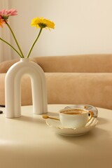 Gerbera flowers and a cup of coffee on a table in a beige bedroom