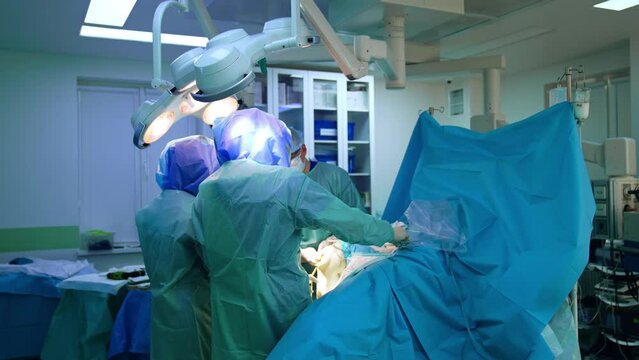 Rear view of two cooperating surgeons performing trauma surgery. Doctors wear protective helmets at procedure.