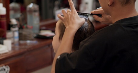 Soft focus Hairdresser cuts hair, combs it. Stylish boy sitting in a hairdresser. Barber man cuts...