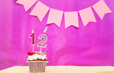 Background date of birth with number  12. Pink background with a cake and burning candles, save space, happy birthday anniversary for a girl. Holiday pudding muffin.
