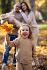 Happy young family with two children dressed in beige colors stands in the park.  The eldest daughter holds leaves in her hands