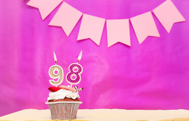Background date of birth with number  98. Pink background with a cake and burning candles, save...