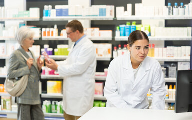 Girl pharmacist in pharmacy works with computer, searches among nomenclature of drugs, specifies price and availability of medicine - obrazy, fototapety, plakaty