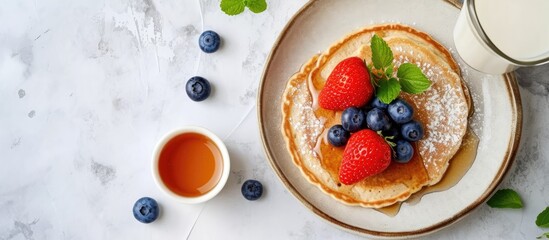 Mini oatmeal pancakes topped with blueberries and strawberries. Pancake porridge in a bowl with milk and maple syrup. Dutch mini pancakes served with milk. Ideal for kids. Milk day celebration.
