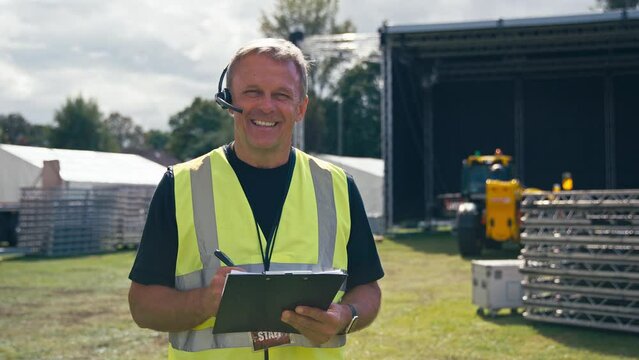 Portrait Of Production Worker With Clipboard Setting Up Outdoor Stage For Music Festival Or Concert
