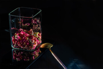 Dry petals and rosebuds in glass jar. Flower tea. Black background. Dried petals and rose buds for...