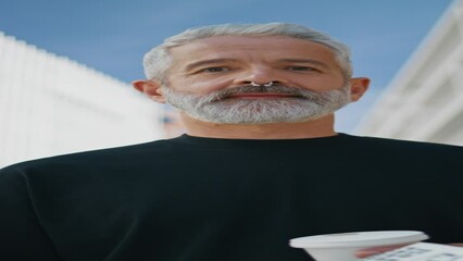 Elderly man looking camera on street vertical closeup. Bearded senior drinking