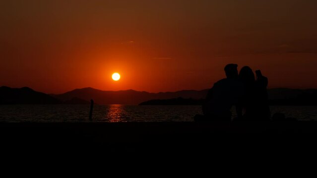 Lovers at sunset. Silhouette of a girl with a guy taking pictures on the phone at sea sunset.