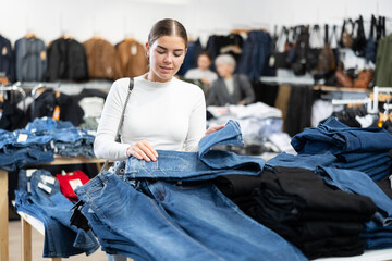 Young woman carefully chooses jeans in a clothing store