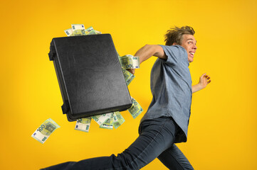 Excited man with roguish grin running away fast carrying a briefcase overstuffed with euro cash, a...