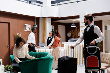 Hotel porter moving suitcase for people, helping guests to find accommodation after front desk...